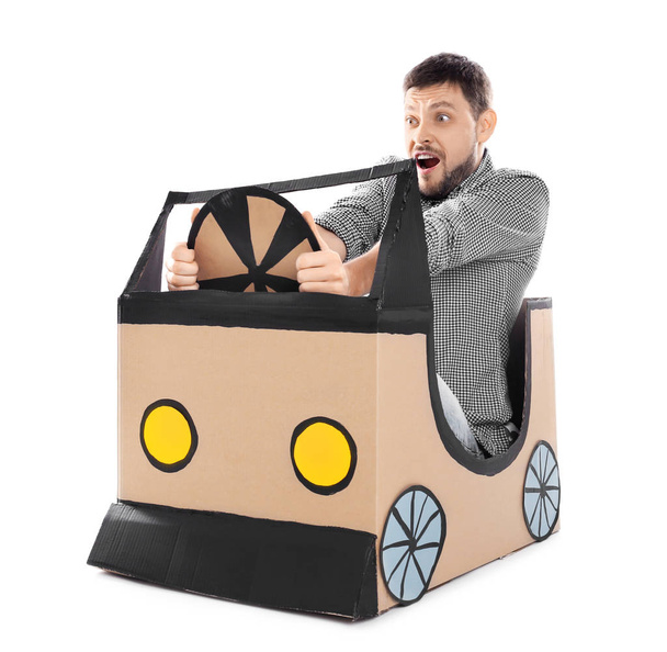 Young man dreaming of buying own auto while playing with cardboard car on white background - Fotó, kép