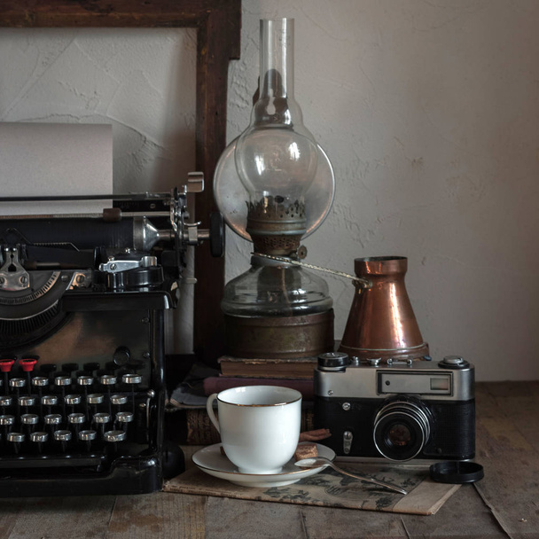 家の内部の静物の詳細。一杯のコーヒー、銅の水差し、ガス灯、書籍、新聞、素朴なスタイルの木製の背景に typewrittert とヴィンテージのレトロなジャーナリスト デスクトップ. - 写真・画像