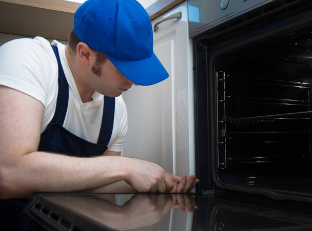 Professional handyman in overalls repairing domestic oven in the kitchen. - Foto, afbeelding