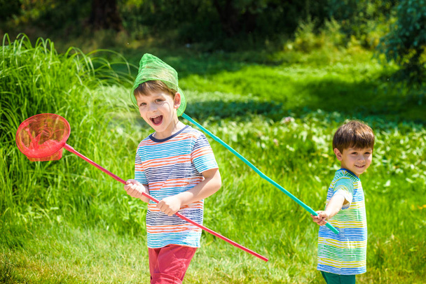 2 人の小さな兄弟兄弟暖かくて日当たりのよい夏や春の日に草原の上スクープ ネットと遊ぶ - 写真・画像