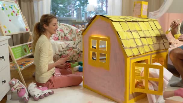 Молода сім'я з дитячим будівництвом та малюванням іграшкового картонного будинку разом
. - Кадри, відео