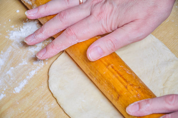 Femme roule la pâte crue de blé avec un rouleau à pâtisserie sur le gâteau plat
 - Photo, image