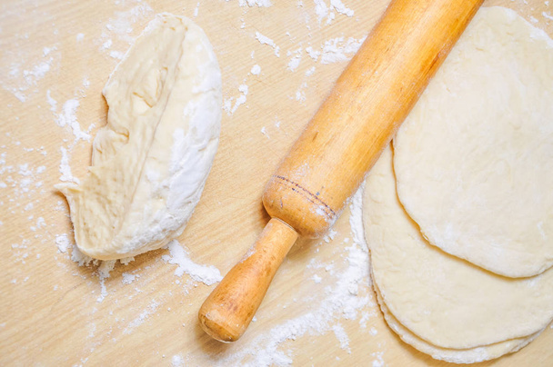 Rolled wheat dough and rolling pin on a wooden table dusted with flour - Фото, изображение