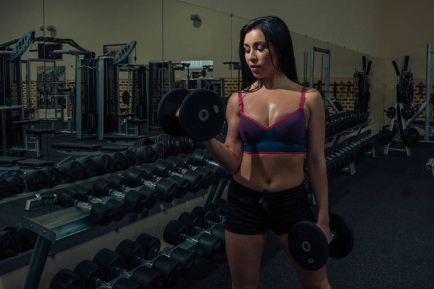 Athletic young woman in sports swimsuit raises dumbbell - Foto, Bild