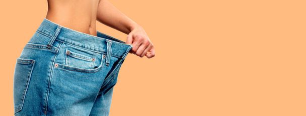 Weight loss. Woman in oversize jeans on pastel background - Foto, Imagen