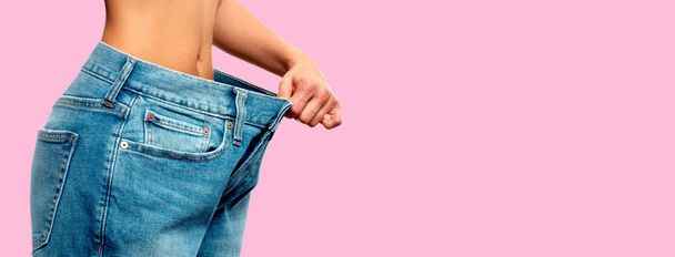 Weight loss. Woman in oversize jeans on pink background - Foto, Bild