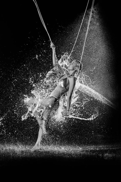 Woman in the water splashes swings on the rope. Black and white. Photographie retouchee - Foto, imagen