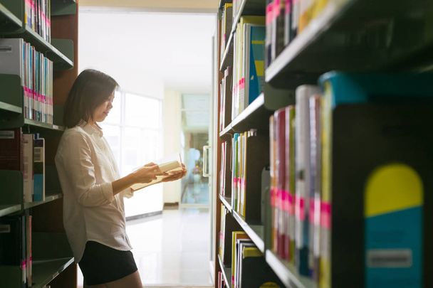 Ασίας φοιτητής διαβάζοντας ένα βιβλίο στη βιβλιοθήκη. - Φωτογραφία, εικόνα