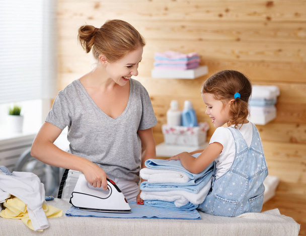 Happy family mother housewife and child daughter ironing clothes - Photo, image