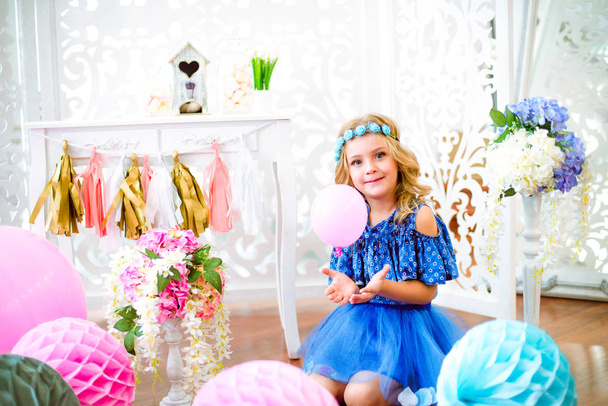 A portrait of a beautiful little girl laughs in a studio decorated many color balloons - 写真・画像