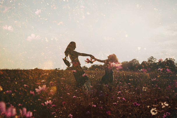 Silhouetten von Mädchen, die Spaß beim Händchenhalten im Blumenfeld haben, Doppelbelichtung - Foto, Bild