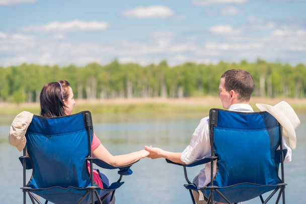 man and woman are sitting on chairs at the pier near the lake an - Photo, Image