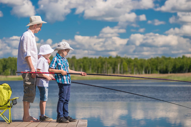 on a wooden pier the father teaches his sons to fish properly - 写真・画像