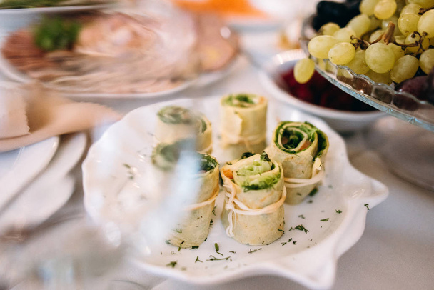 Schließen Sie die Pfannkuchenrollen mit Lachs und Spinat gebunden mit armenischem geflochtenen Saitenkäse auf weißem Teller serviert - Foto, Bild