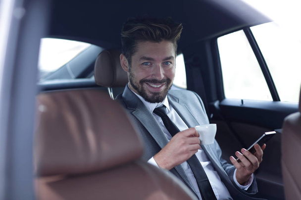 Businessman drinking coffee in car with phone in hand - Zdjęcie, obraz
