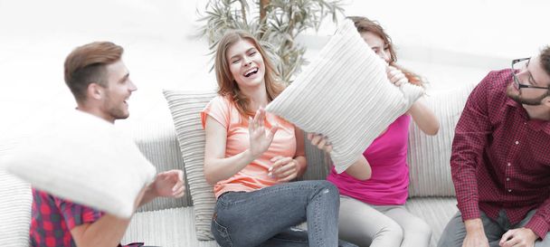 cheerful friends playing with the pillows sitting on the couch - Фото, изображение