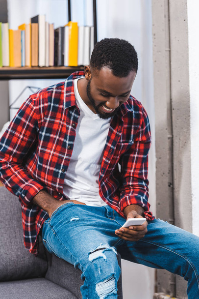sourire jeune homme afro-américain en utilisant un smartphone à la maison
 - Photo, image