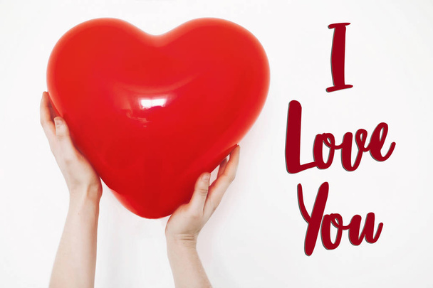 Ik hou van je tekst teken. Happy valentine's day concept. hand met rood hart ballon op witte achtergrond met ruimte voor tekst. wenskaart - Foto, afbeelding