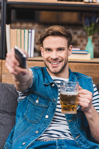 smiling young man holding glass of beer and remote controller - Foto, immagini