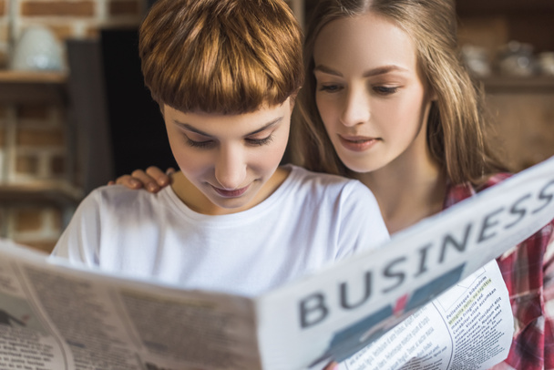 close-up portrait of young lesbian couple reading newspaper together - Photo, Image