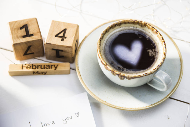 Serce znajduje odzwierciedlenie w filiżance kawy na stoliku obok drewniane kalendarza. Koncepcja Walentynki - Zdjęcie, obraz