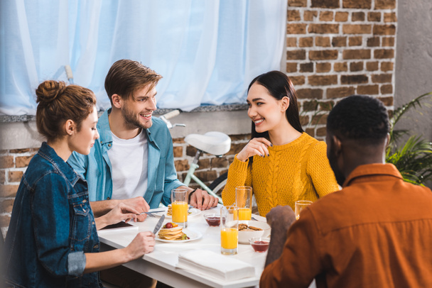 щасливі молоді багатоетнічні друзі їдять сніданок і розмовляють за столом
 - Фото, зображення