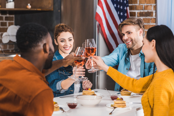 happy young multiethnic friends clinking wine glasses above table - Photo, Image