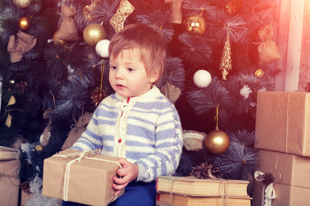 Little boy holds Christmas present near fir tree - Photo, Image