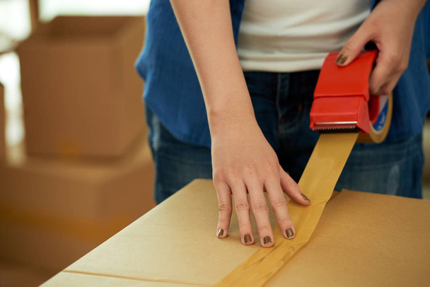 vista parcial de la mujer embalaje cosas en caja de cartón y el uso de cinta adhesiva para mover
 - Foto, imagen