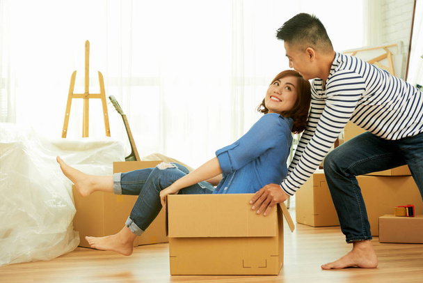 juguetón asiático hombre llevar mujer en caja mientras casa moviéndose
 - Foto, imagen