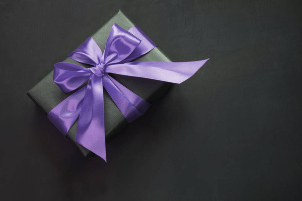 Gift box in black paper with ultra violet ribbon on black surface. Top view. - Foto, immagini