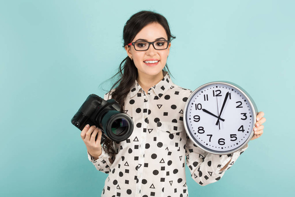 Joven morena sosteniendo cámara fotográfica profesional y reloj de pared
 - Foto, Imagen