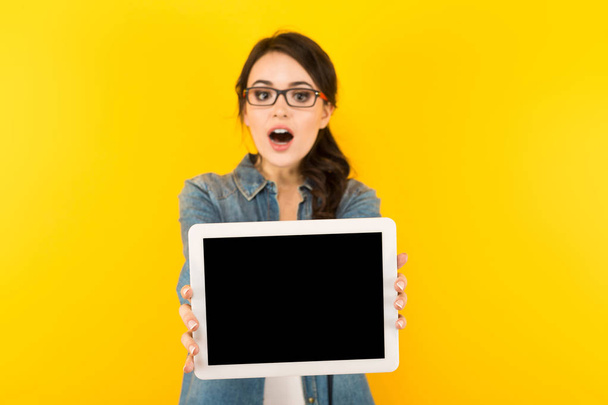 überraschte junge brünette Frau zeigt digitales Tablet mit leerem Bildschirm - Foto, Bild