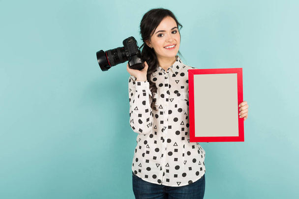 Jeune femme brune tenant un appareil photo et un cadre vide et souriant à la caméra
 - Photo, image