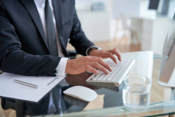 visão parcial do empresário digitando no teclado do computador na mesa no escritório
 - Foto, Imagem