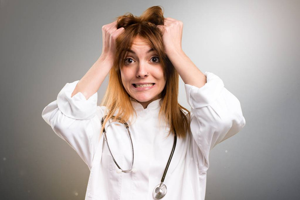 Mujer joven médico frustrado sobre fondo gris
 - Foto, Imagen