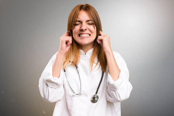 Νέος γιατρός γυναίκα που καλύπτουν τα αυτιά της σε γκρίζο φόντο - Φωτογραφία, εικόνα