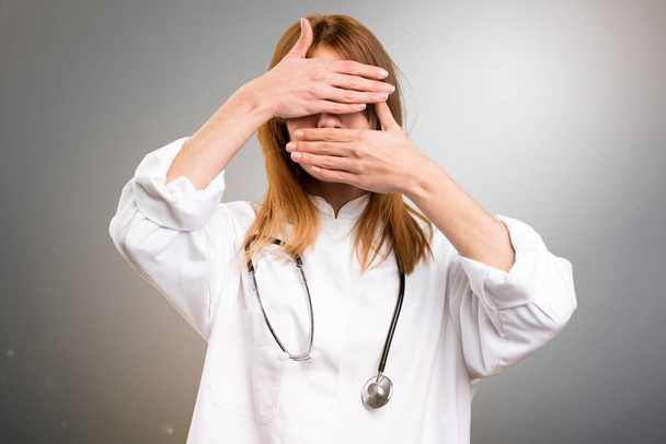 Молода лікарка, що прикриває обличчя на сірому фоні
 - Фото, зображення