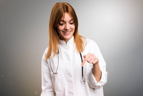 Mladý lékař žena směřující dolů na šedém pozadí - Fotografie, Obrázek