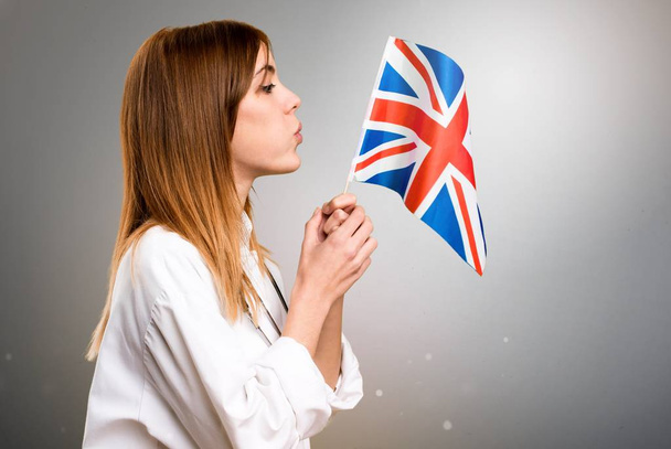 junge Ärztin mit einer Flagge des Vereinigten Königreichs auf grauem Hintergrund - Foto, Bild