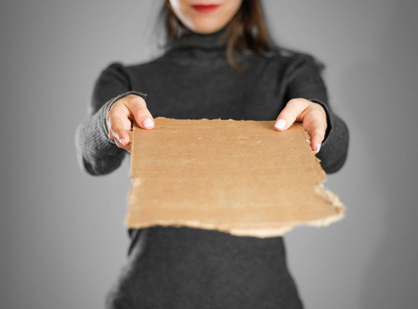 A young girl in a grey jacket holding a piece of cardboard. Prep - Zdjęcie, obraz