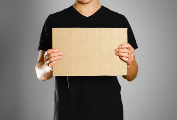 A young guy in a black t-shirt holding a piece of cardboard. Pre - Foto, Imagem