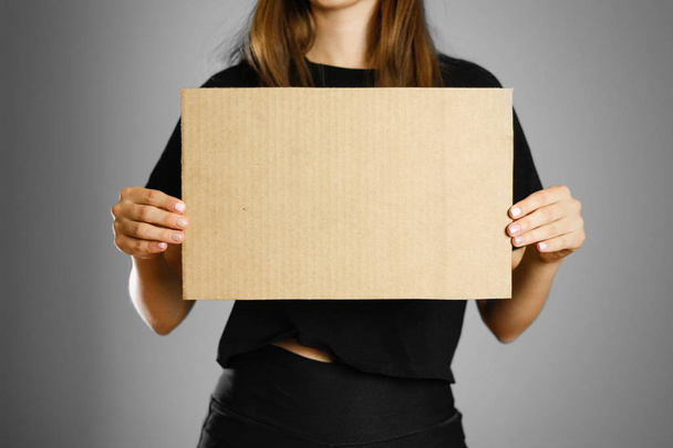 A young girl in a black t-shirt holding a piece of cardboard. Pr - Foto, Imagem