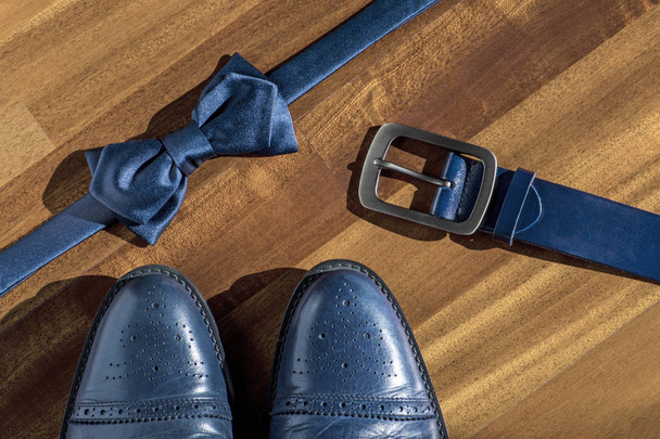 Composición con elegantes zapatos hechos a mano de cuero azul para hombre, cinturón y pajarita sobre fondo de madera
 - Foto, Imagen