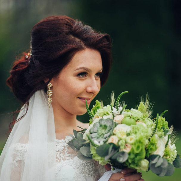 attractive caucasian bride with flowers posing in park - Photo, image