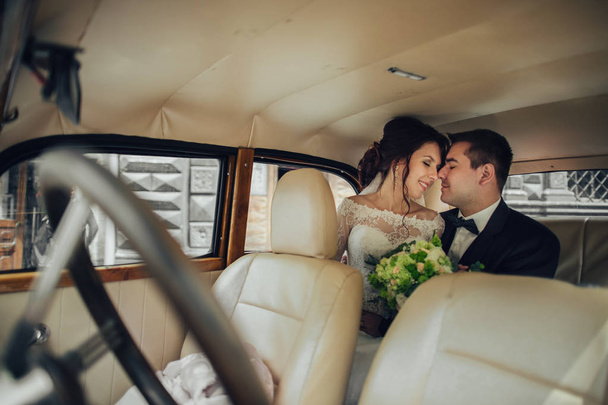young attractive caucasian wedding couple with flowers bouquet hugging in retro car - Foto, Imagem