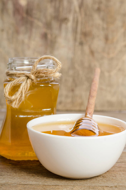 a jar of honey and bowl with honey isolated on wooden background - Photo, Image