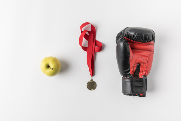 вид сверху боксерской перчатки с медалью и зеленым яблоком на белой поверхности
 - Фото, изображение