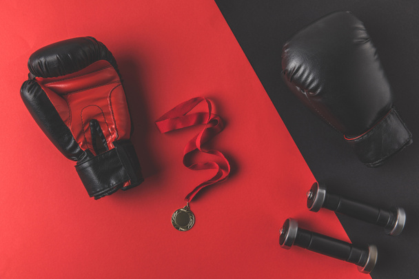 вид сверху боксерских перчаток с медалью и гантелями на красной и черной поверхности
 - Фото, изображение