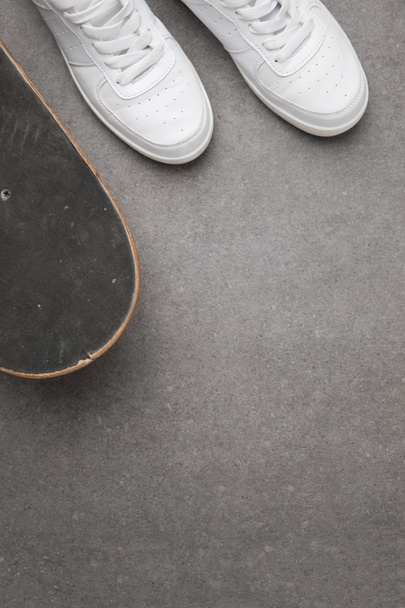 вид сверху на белые кроссовки и скейтборд на серой асфальтовой поверхности
 - Фото, изображение